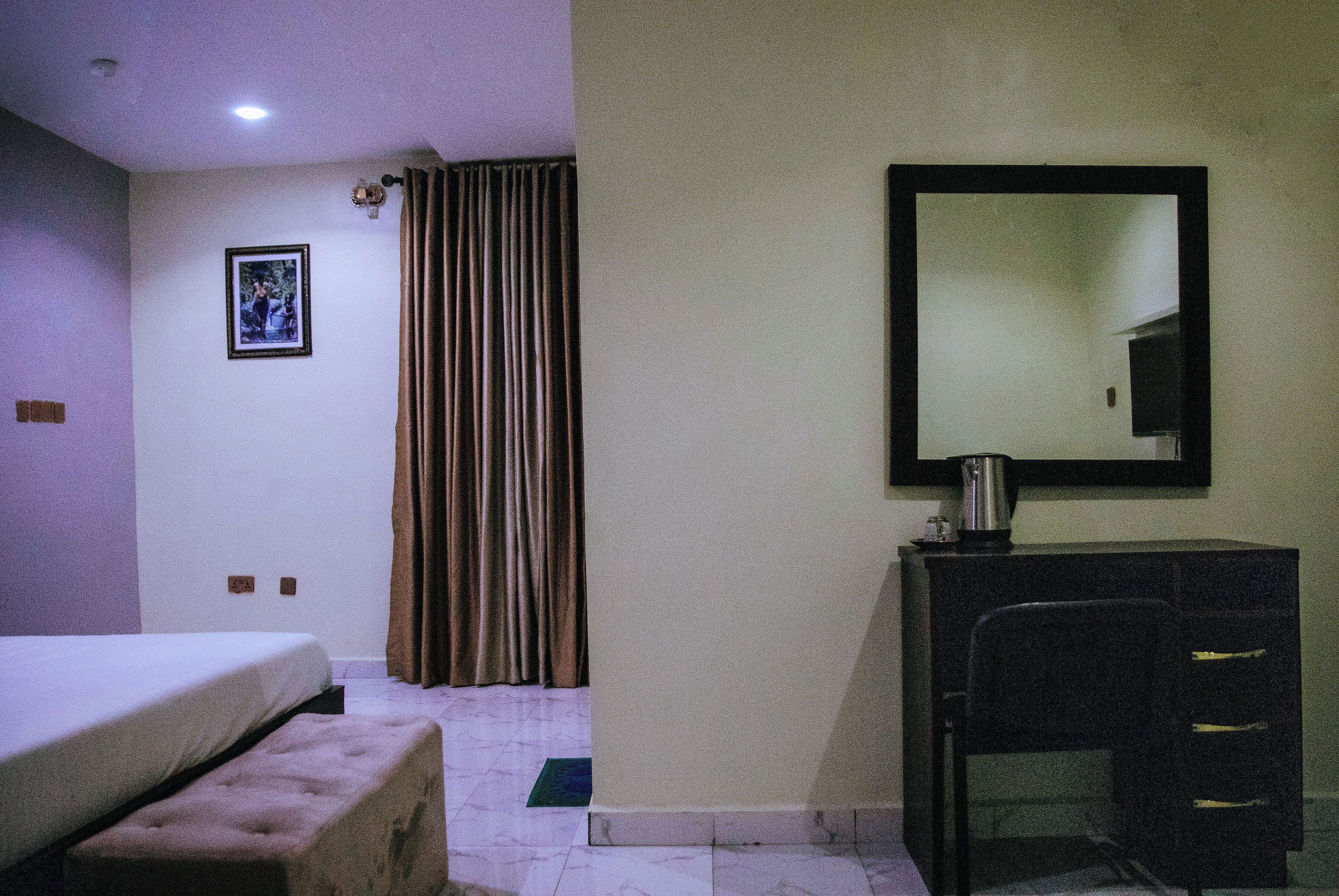 A hotel room with a bed, a desk, a chair, a mirror, a picture on the wall, and a curtain.
