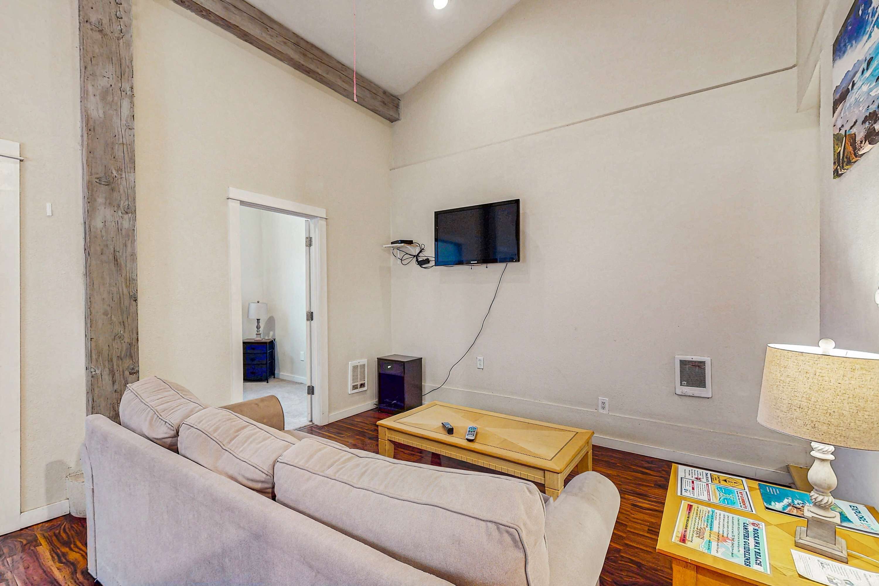 Una sala de estar con sofá, una mesa de centro, un televisor montado en la pared y una lámpara.