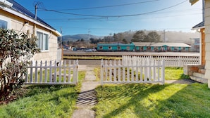 Un barrio residencial con cerca blanca en forma de piquete, un sendero que lleva a una casa y una estación de tren al fondo.