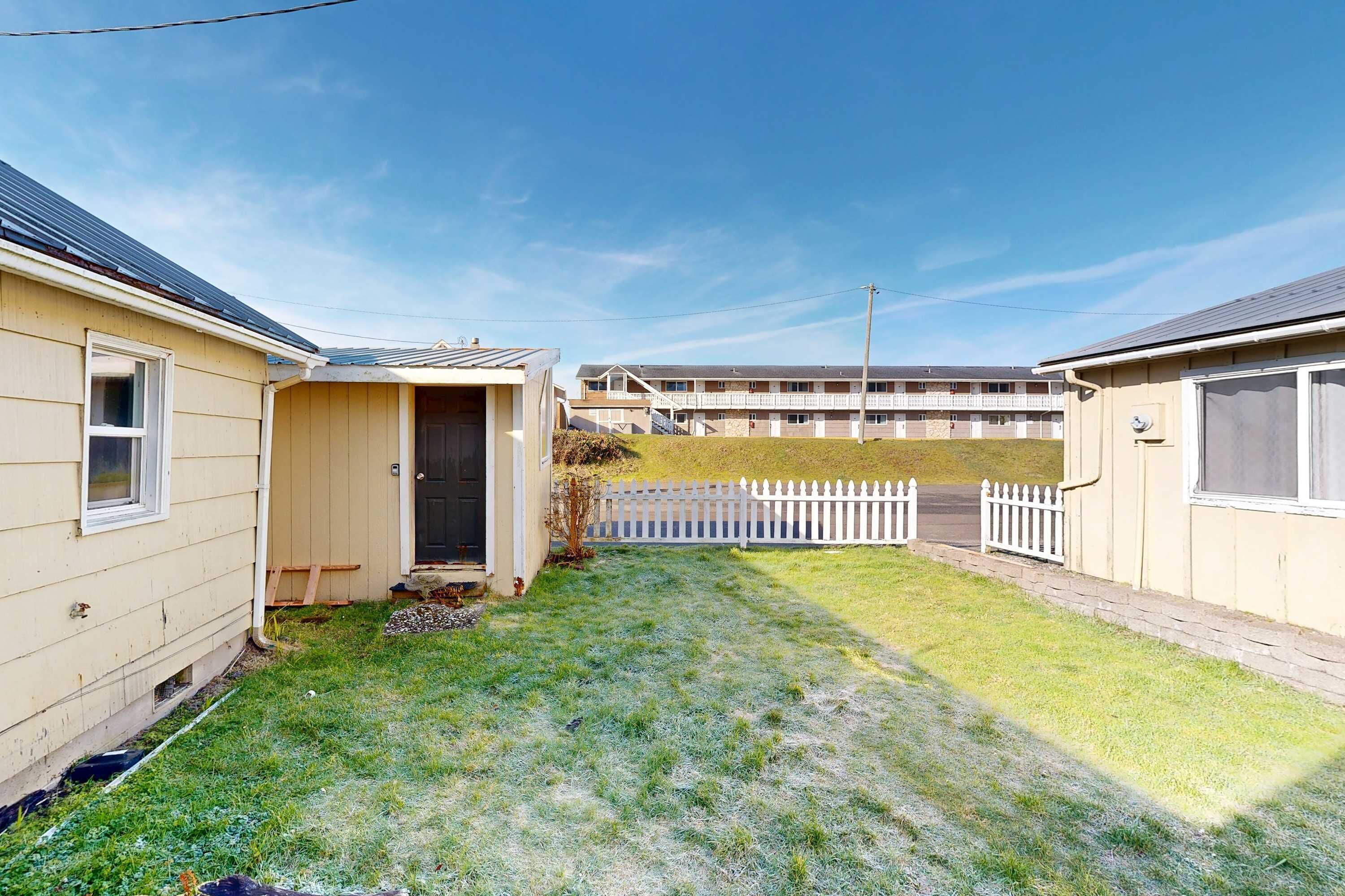 A residential area with two single-story houses, a small yard, and a white picket fence.