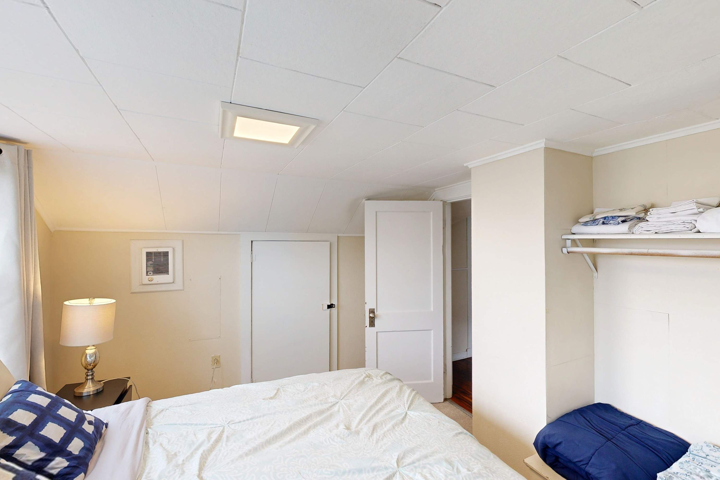 Een hotelkamer met een bed, een nachtkastje met een lamp, een kledingkast en een plank met opgevouwen kleding.