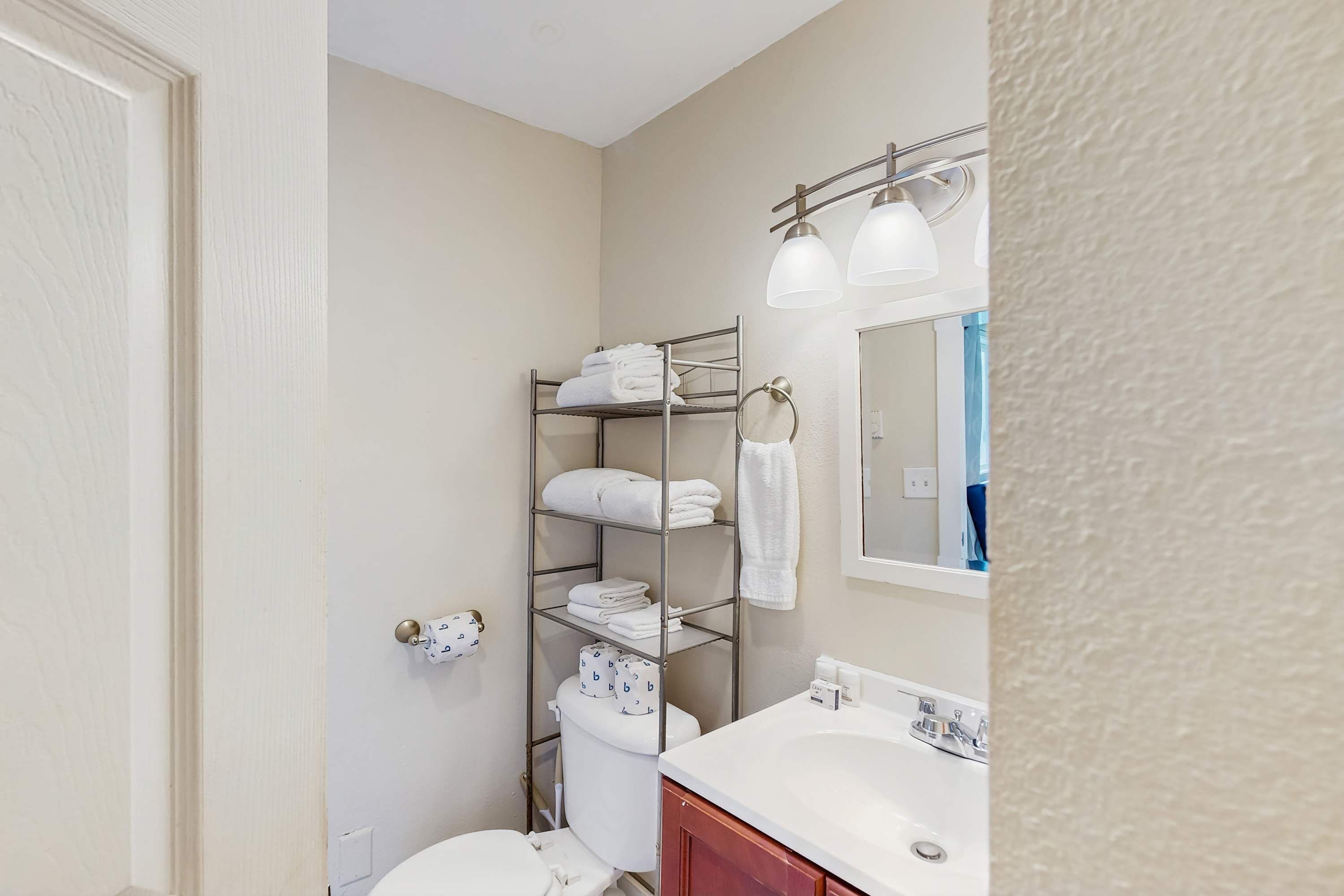 A bathroom with a white sink, a toilet, a towel rack, and a shelf with towels.