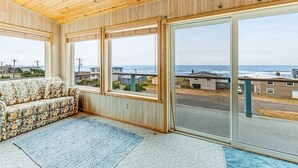 Ein Zimmer mit Holzboden, einem gemusterten Sofa und großen Fenstern mit Blick auf das Meer und umliegende Gebäude.
