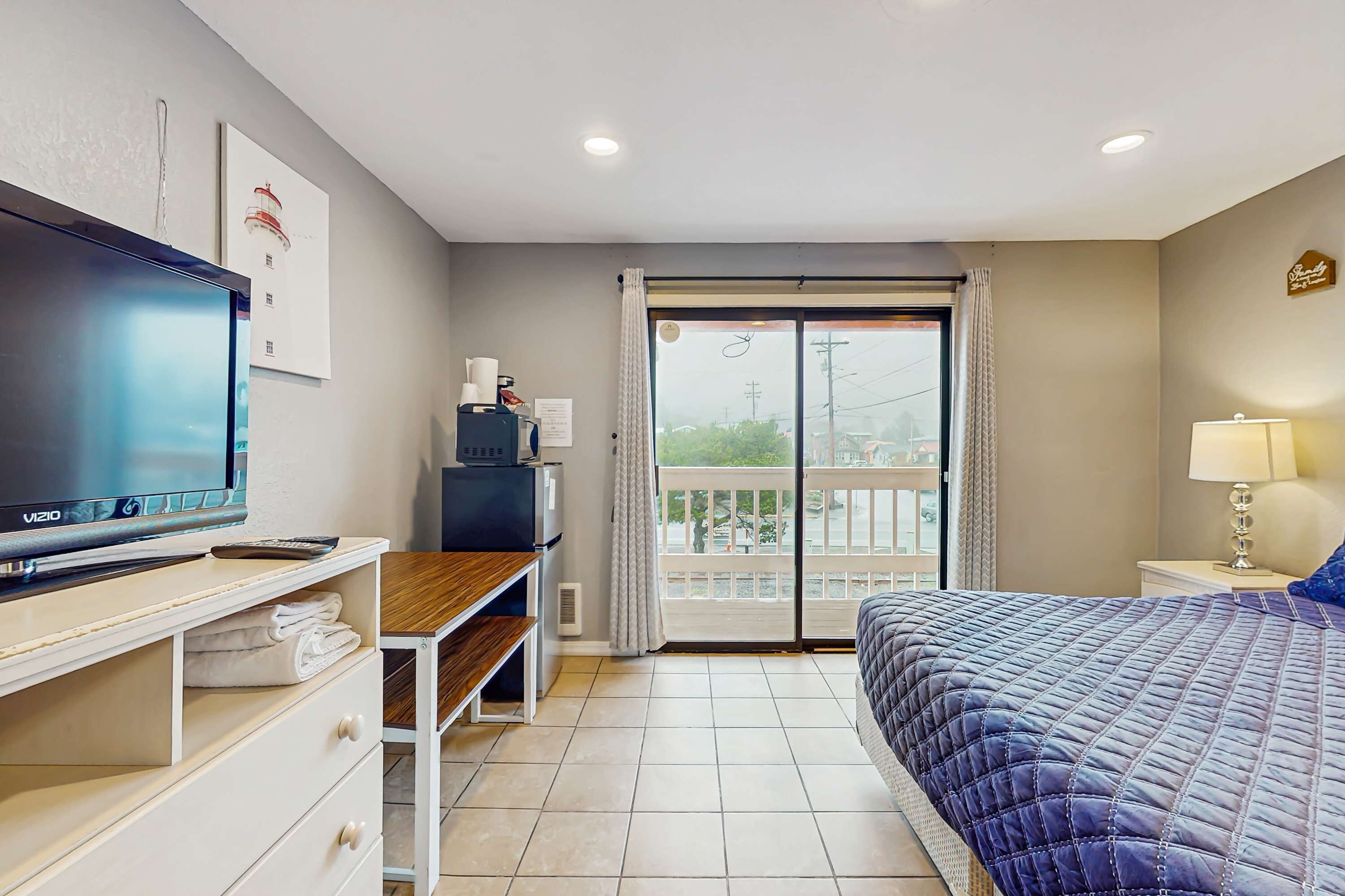 A hotel room with a bed, a TV, a desk, and a balcony with a view.