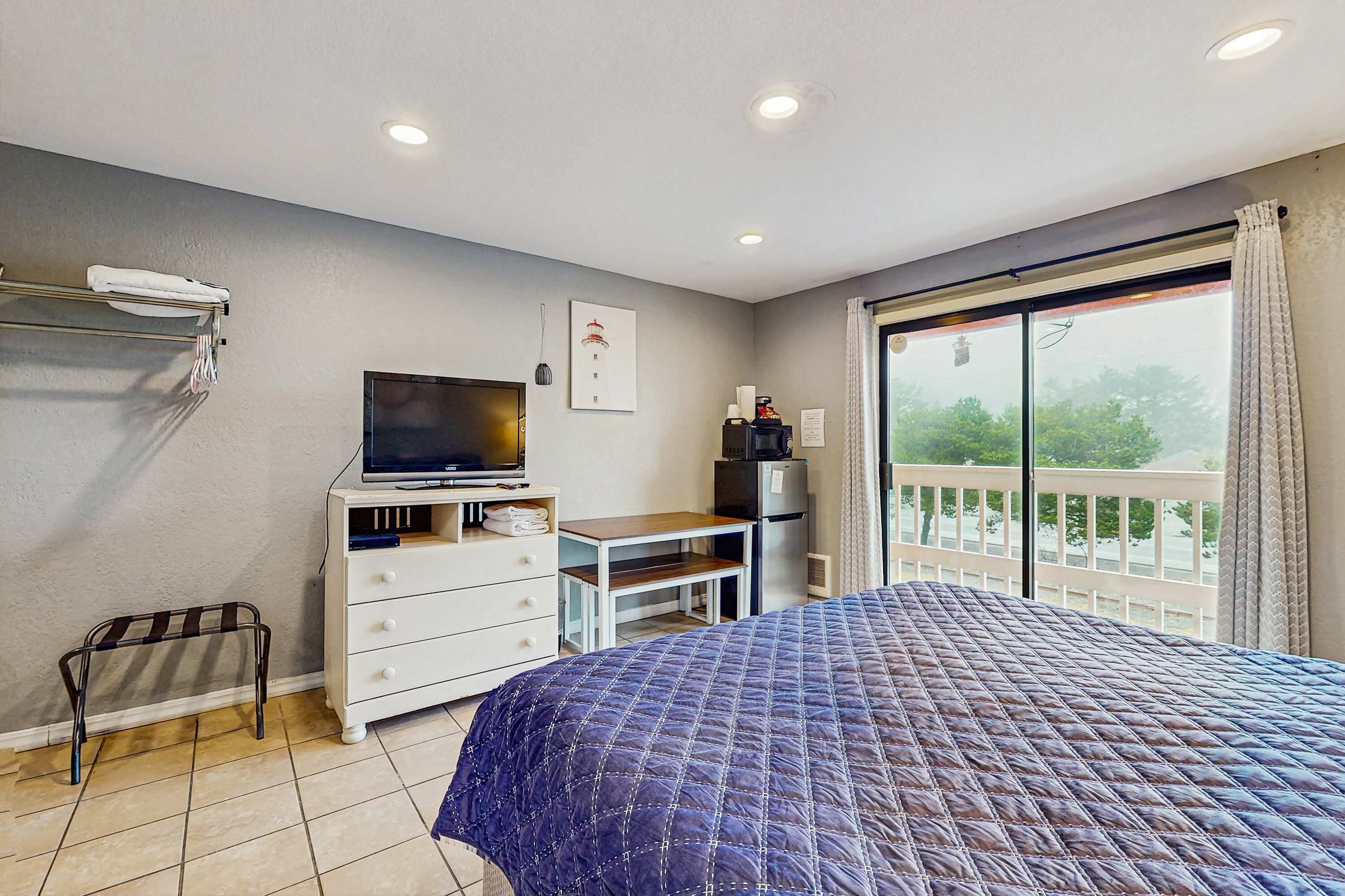 A bedroom with a bed, a TV, a desk, and a balcony with a view.