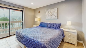 A bedroom with a large bed, two bedside tables with lamps, a wall art piece, and a view through a sliding door. - Dog Friendly Room Located Near the Beach and Downtown (Rockaway Beach)