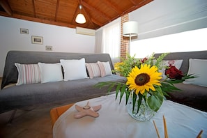 A cozy room with a grey sofa, a small table with a starfish decoration, and a vase with sunflowers and a red rose.