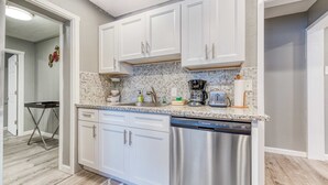 A modern kitchen with white cabinets, a stainless steel dishwasher, and a tiled backsplash. - Dog friendly motel with kitchens and kitchenettes and WiFi walk to the beach (Rockaway Beach)