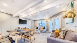 A modern living room with a dining area, a sofa, and a TV mounted on the wall. - Dog friendly motel with kitchens and kitchenettes and WiFi walk to the beach (Rockaway Beach)
