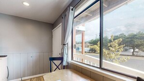 Une pièce avec une grande fenêtre, une table en bois, une chaise et un meuble blanc.