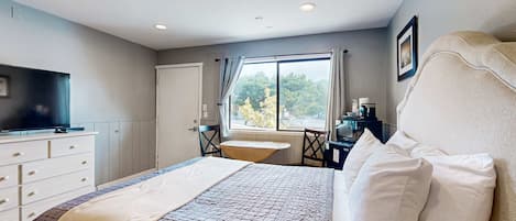Makuuhuoneessa on sänky, lipasto, televisio, ikkuna, jossa on verhot, sekä työpöytä ja tuoli.