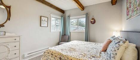 A bedroom with a bed, dresser, and a window with curtains.