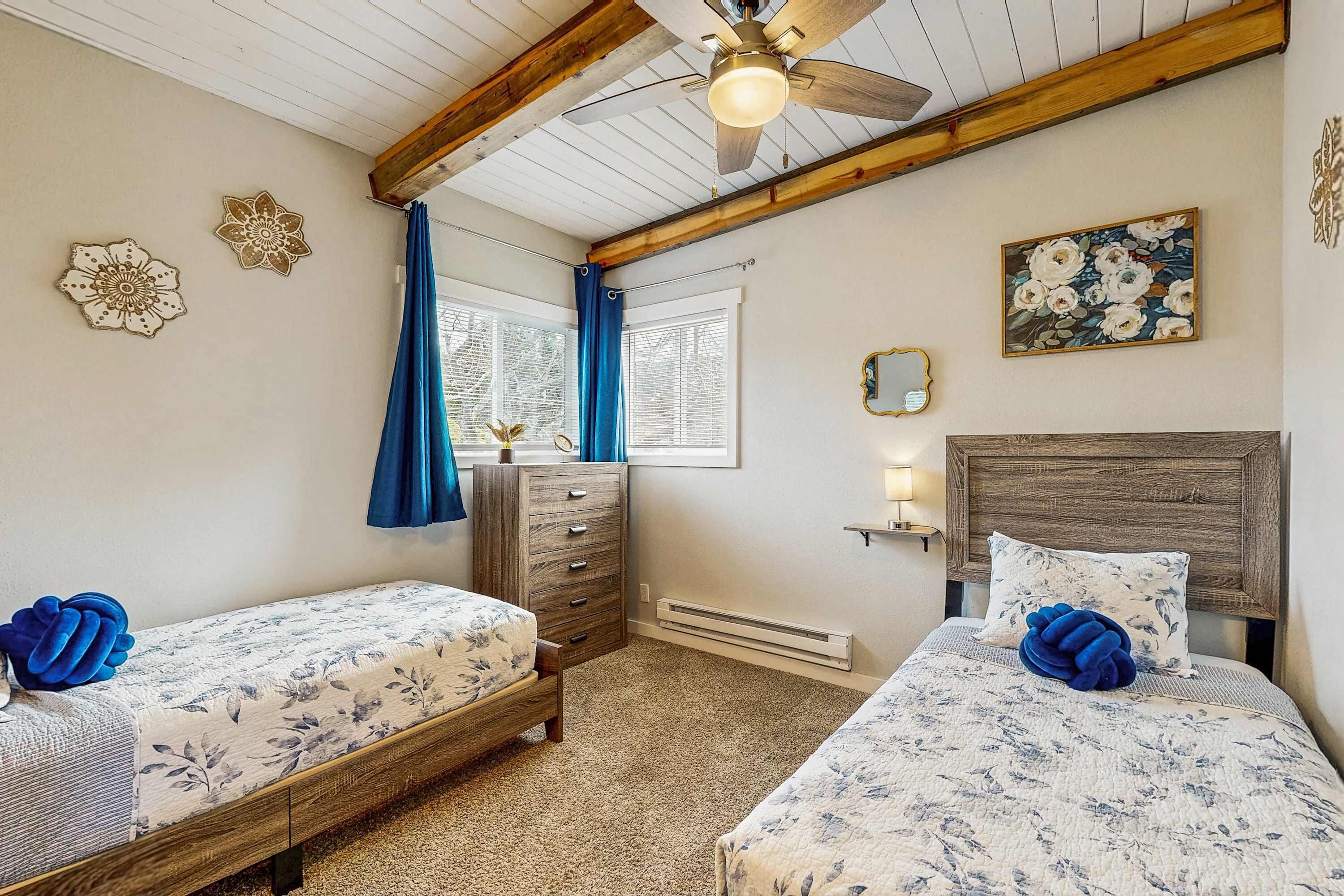 A bedroom with two beds, a dresser, a ceiling fan, and a window with curtains.