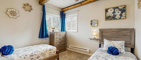 A bedroom with two beds, a dresser, a ceiling fan, and a window with curtains.
