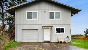 Ein zweistöckiges Haus mit Garage, Eingangstür und einer kleinen Veranda mit zwei Stühlen.