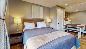 A bedroom with a large bed, two bedside tables with lamps, a wooden bench, and a door leading to another room. - Classy Dog Friendly Studio with Free WiFi and Cable Walk to the Beach (Rockaway Beach)