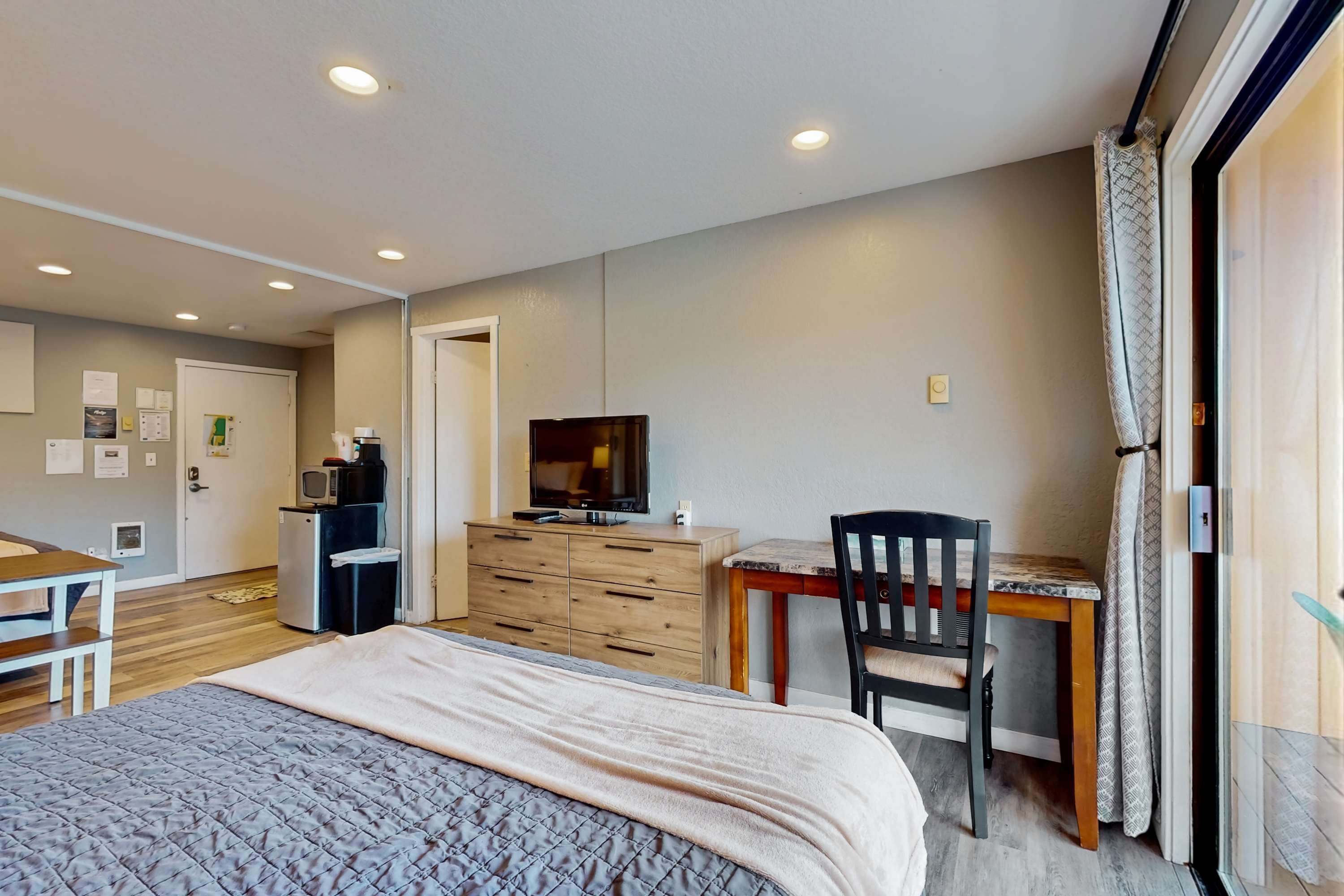 A bedroom with a bed, a desk, a chair, a TV, and a dresser.