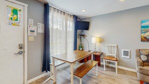 A room with a wooden table, bench, white chairs, a TV mounted on the wall, and a painting. - Dog Friendly Room with Kitchen Located Near the Beach and Downtown (Rockaway Beach)