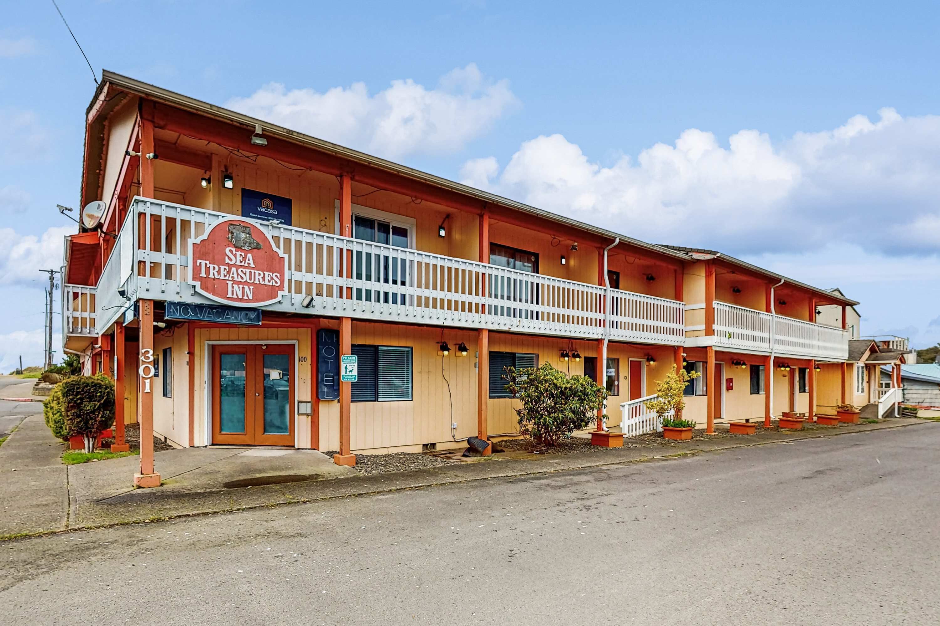 Un motel à deux étages avec un balcon au rez-de-chaussée, une enseigne indiquant « Sea Treasures Inn » et une porte d’entrée bien visible.