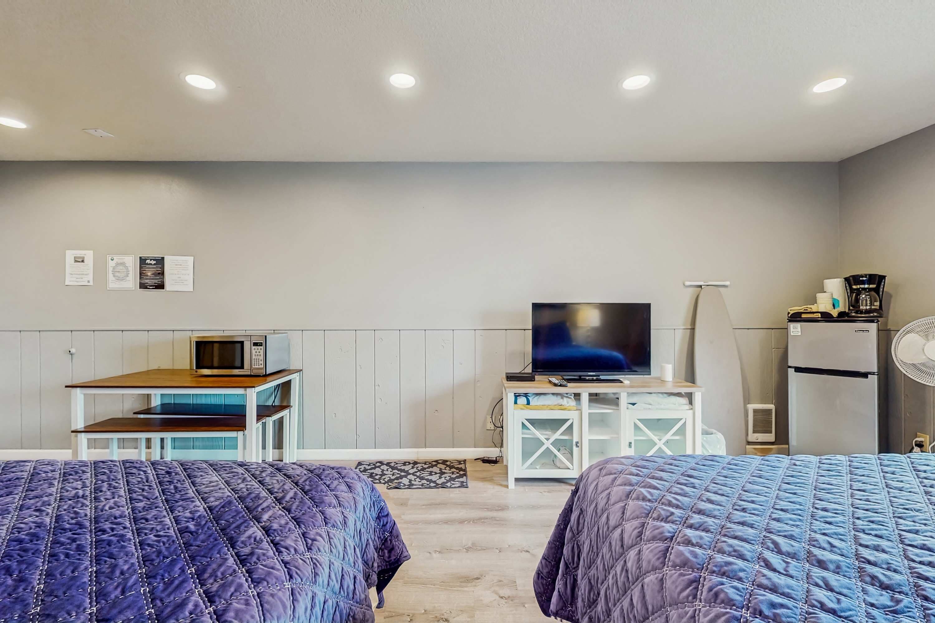 Habitación de hotel con dos camas, televisión, microondas, refrigerador y una pequeña mesa con una silla.