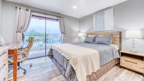 Un dormitorio con cama, escritorio, silla y vistas al balcón.