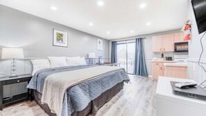 A modern hotel room with a large bed, a desk with a laptop, a flat-screen TV, and a kitchen area. - Dog Friendly Room with Kitchen Located Near the Beach and Downtown (Rockaway Beach)