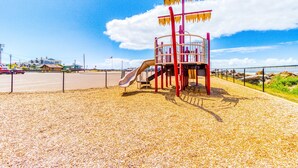 A playground with a slide and climbing structures, surrounded by a fence and a sandy ground. - Dog Friendly Room with Kitchen Located Near the Beach and Downtown (Rockaway Beach)
