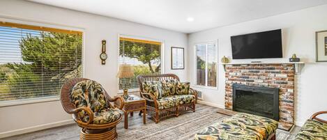Una sala de estar con chimenea, muebles de mimbre y ventanas grandes.