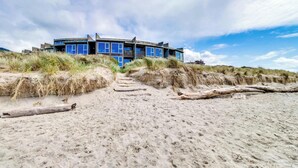 Een modern strandhuis met een plat dak, grote ramen en een zandstrand op de voorgrond.