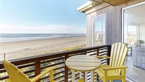 Een balkon met uitzicht op het strand, een ronde tafel en twee gele stoelen.