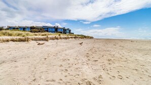 Een strandpand met een modern ontwerp, bestaande uit een reeks verbonden gebouwen met grote ramen, gelegen aan een zandstrand met duidelijke voetafdrukken.