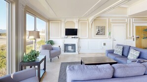 Een ruime woonkamer met een open haard, een televisie en een groot raam met uitzicht op de omgeving.