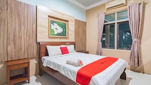 A hotel room with a wooden bed, a nightstand, a window with curtains, and a wall-mounted air conditioner. - Sangkan Hurip Kuningan Hiyel (Cilimus)