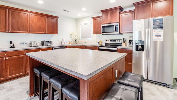 A kitchen with wooden cabinets, a stainless steel refrigerator, a microwave, and a large island with bar stools.