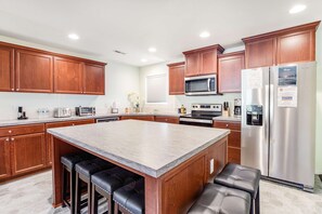 Una cocina con armarios de madera, un refrigerador de acero inoxidable, un microondas y una isla grande con taburetes de bar.