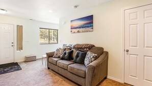 A living room with a beige carpet, a gray sofa with patterned cushions, a window, and a door.