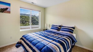 A bedroom with a large bed, a window with a view of trees, and a painting on the wall.