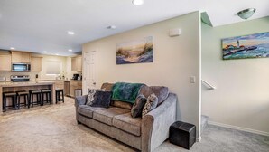 A living room with a sofa, a coffee table, and a kitchen area with a microwave and bar stools.