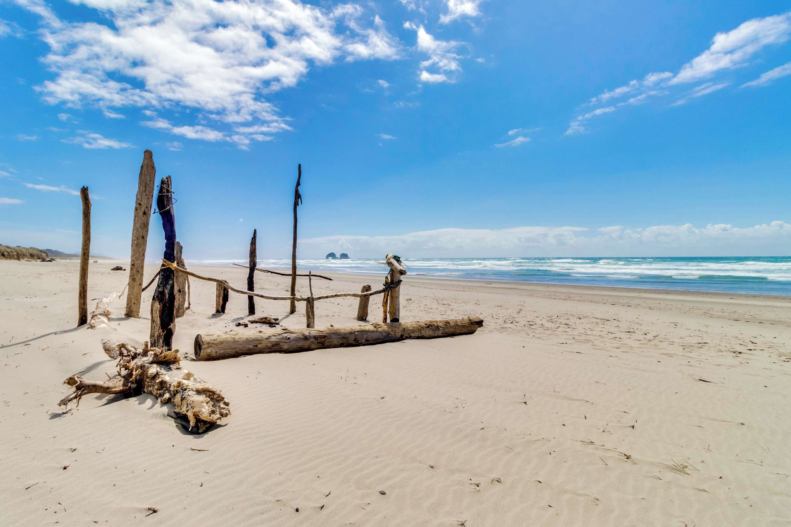 Una playa arenosa con postes de madera y una cerca de cuerda.