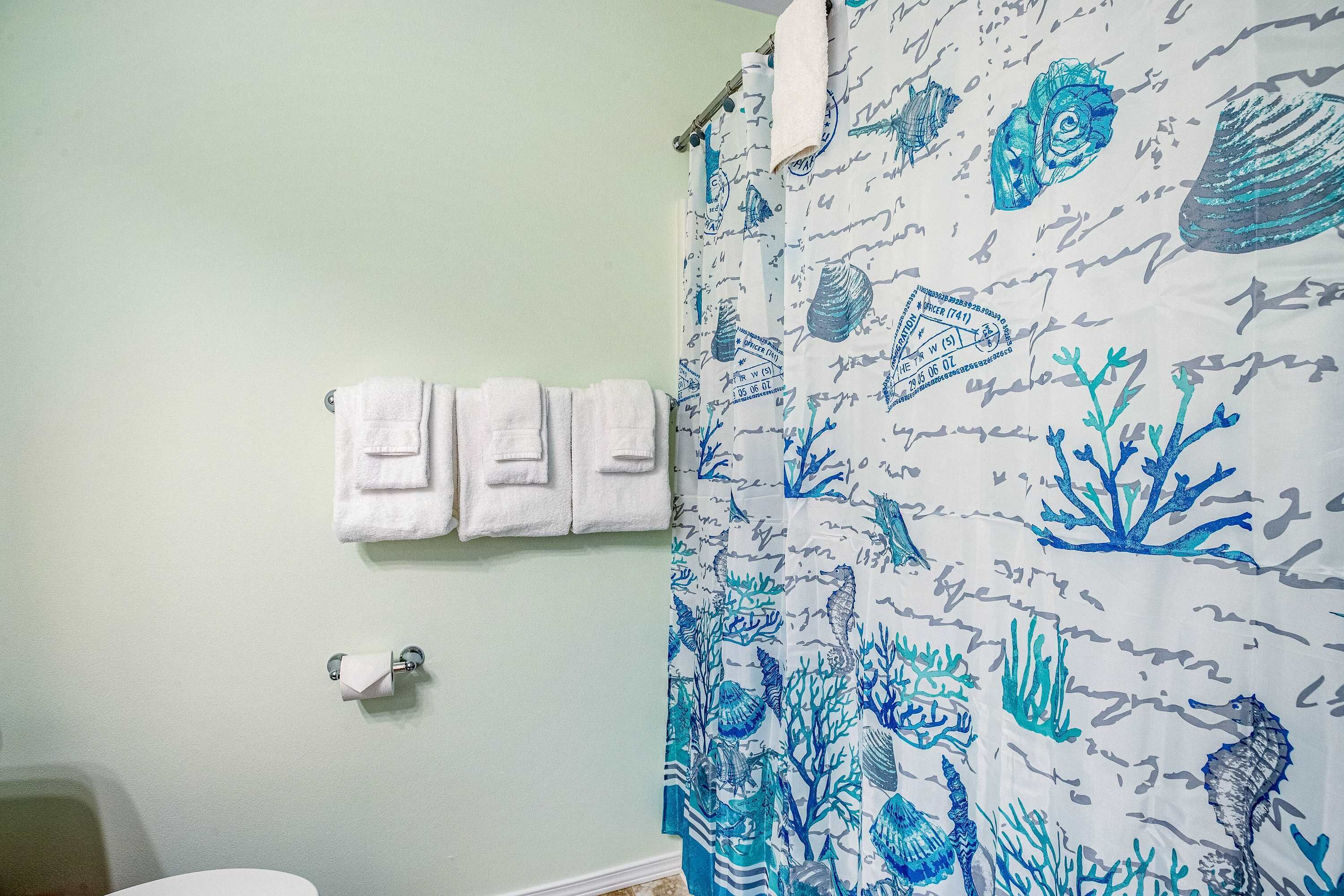 Um banheiro com cortina de chuveiro estampada com um padrão náutico em azul e branco, um porta-toalhas com três toalhas e um rolo de papel higiênico.