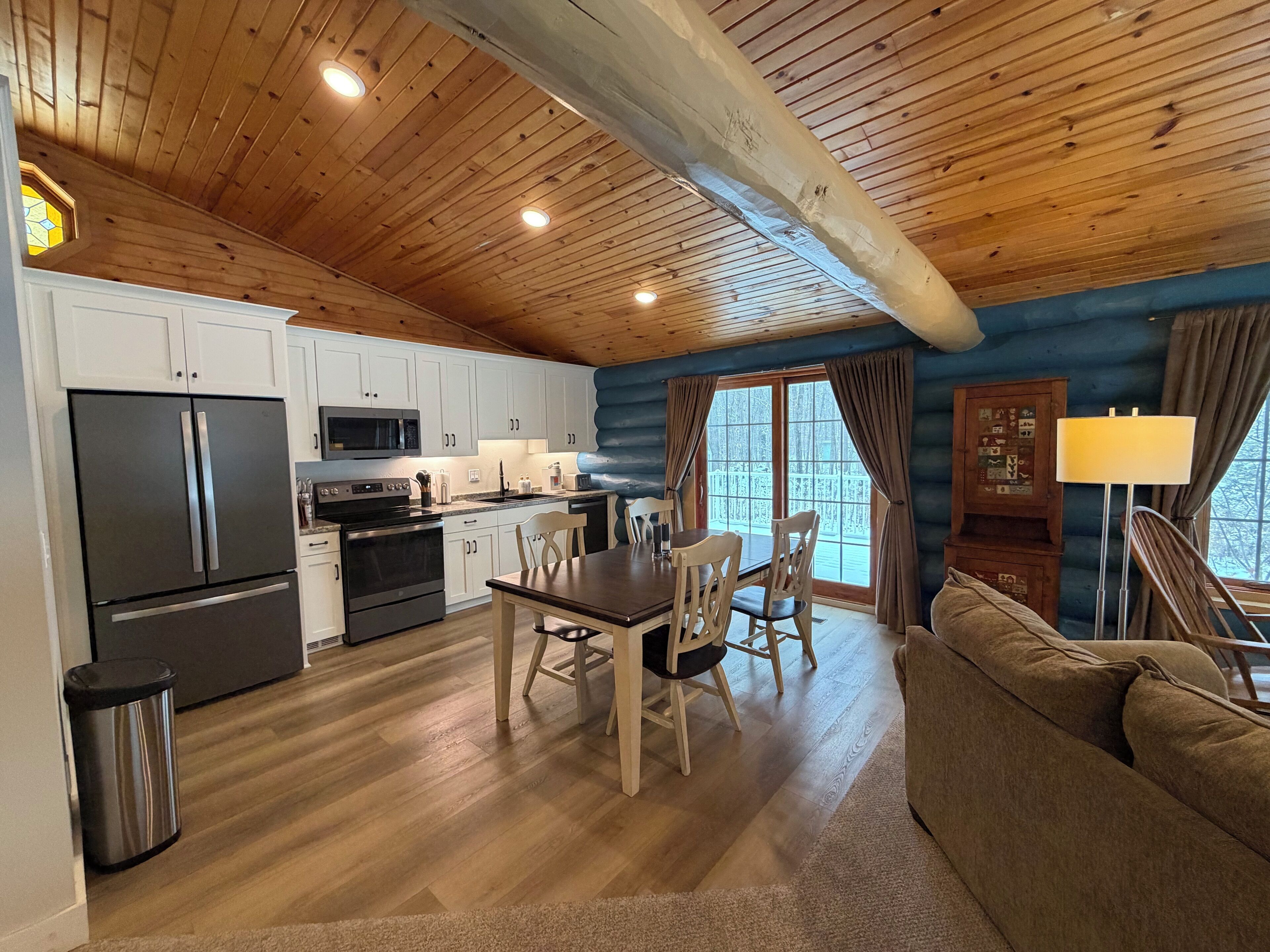 Cocina acogedora de estilo cabaña, con techos de madera, armarios blancos y un comedor con mesa y sillas.