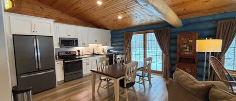 Cocina acogedora de estilo cabaña, con techos de madera, armarios blancos y un comedor con mesa y sillas.