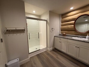 A modern bathroom with a glass shower enclosure, a vanity with a sink, and a wooden log wall. - Fabulous Log Suite in charming Ephraim (Sister Bay)