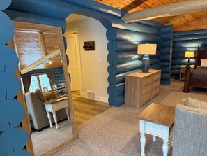 A log cabin interior with a cozy living area, a wooden dresser, a lamp, and a bed. - Fabulous Log Suite in charming Ephraim (Sister Bay)