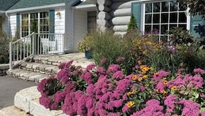 Une cabane en rondins avec un escalier en pierre menant à un porche, le tout entouré de fleurs aux couleurs vives.