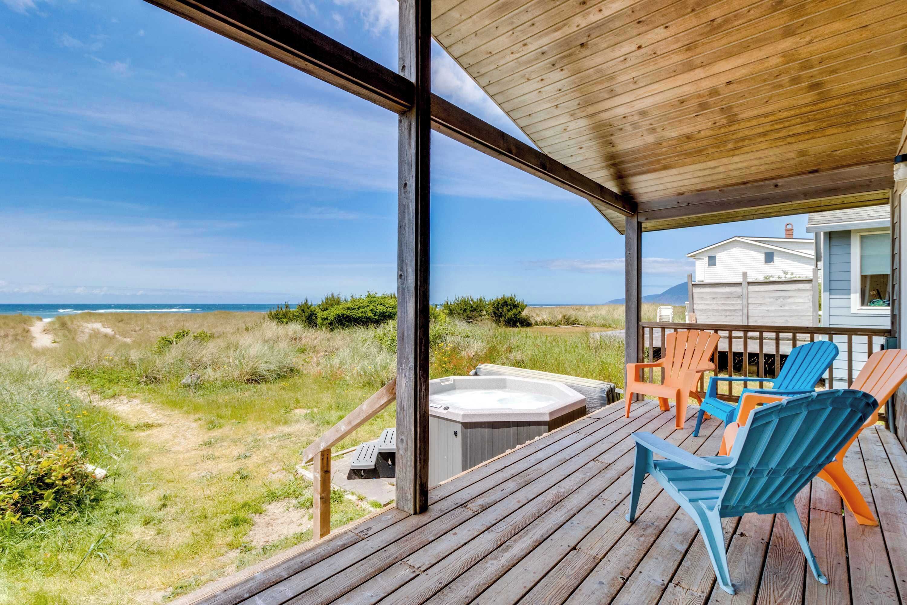 Une terrasse en bois avec un jacuzzi et des fauteuils Adirondack donnant sur une plage.