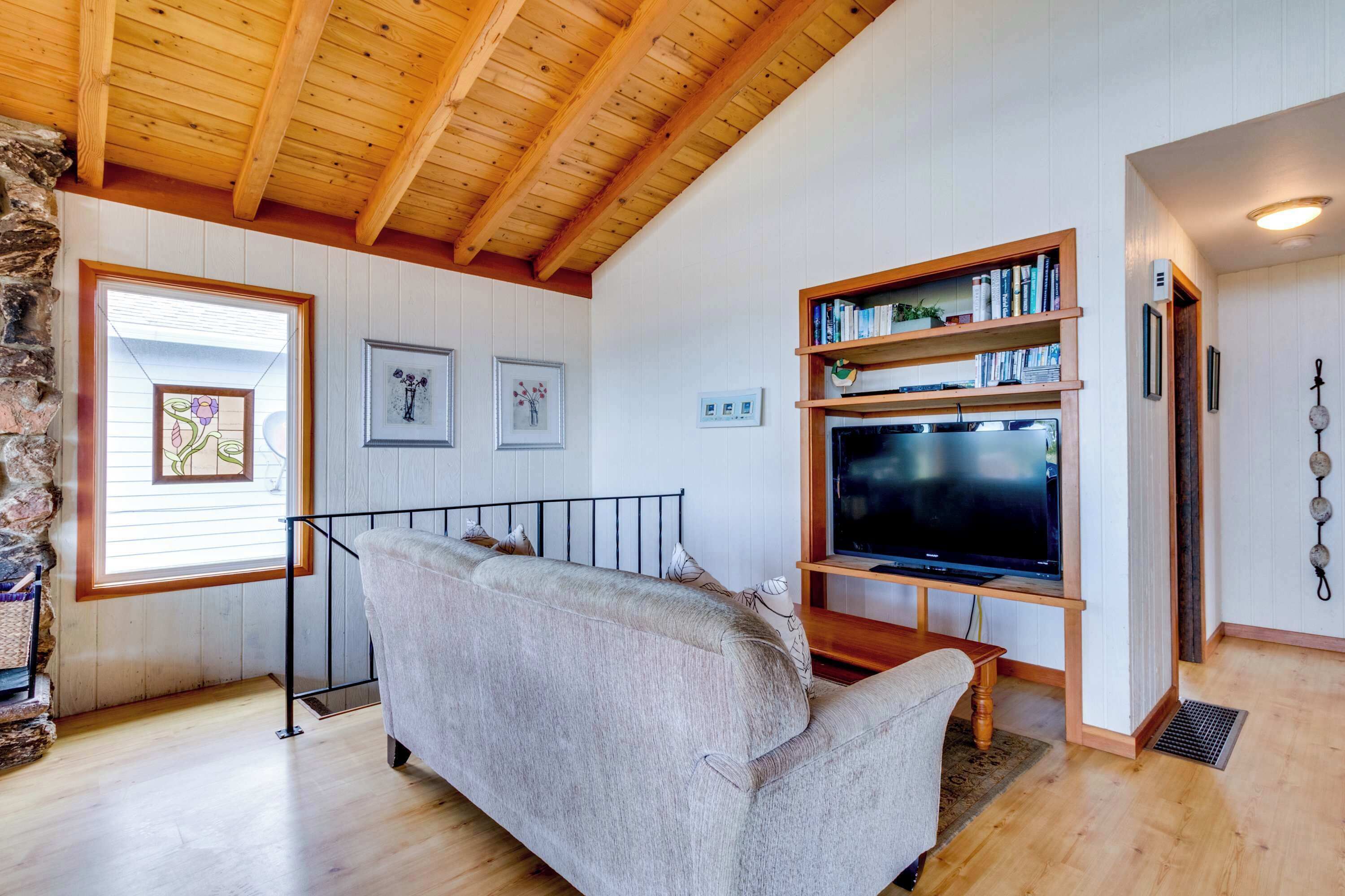 Una sala de estar acogedora con techo de madera, un sofá, un televisor sobre un mueble de madera y una estantería.