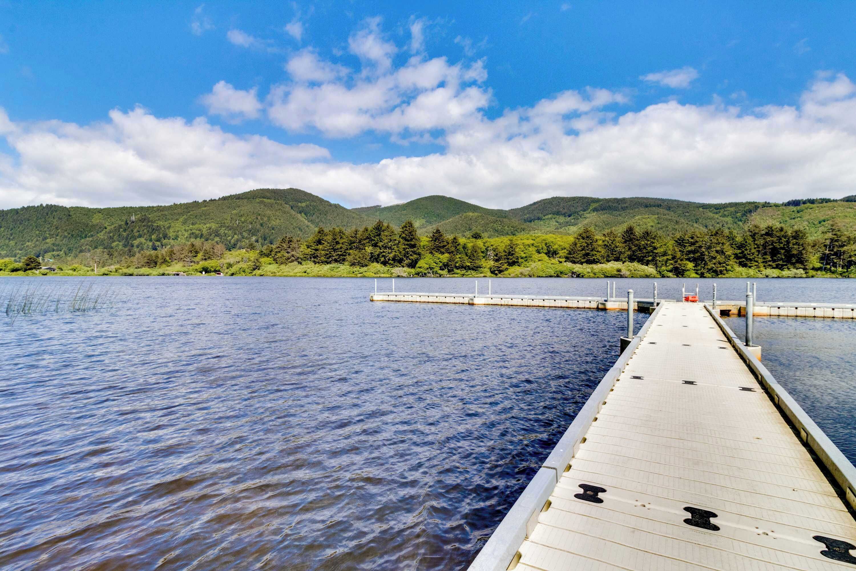 A wooden pier extending into a calm lake, surrounded by lush green hills under a partly cloudy sky.