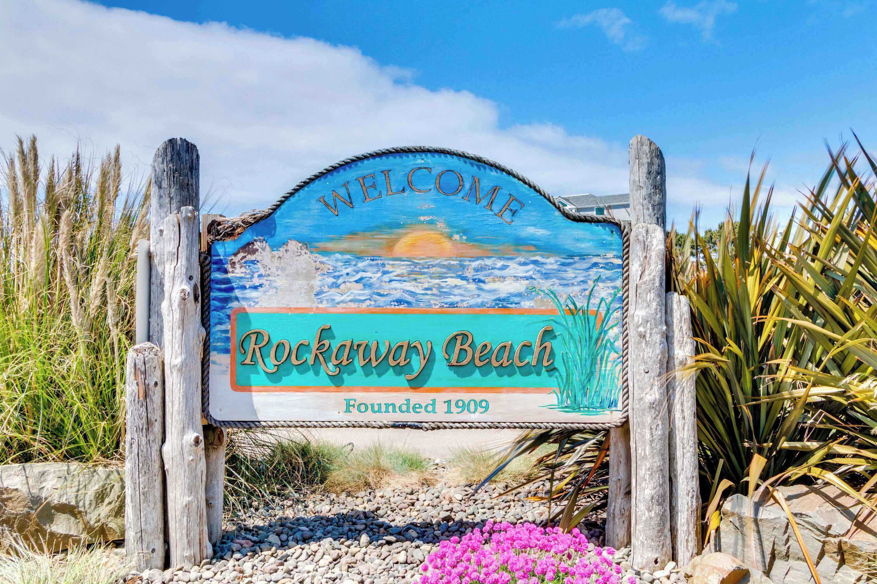 A welcome sign for Rockaway Beach with a coastal scene and the text "Welcome Rockaway Beach Founded 1909".