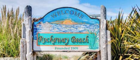 A welcome sign for Rockaway Beach with a coastal scene and the text "Welcome Rockaway Beach Founded 1909".